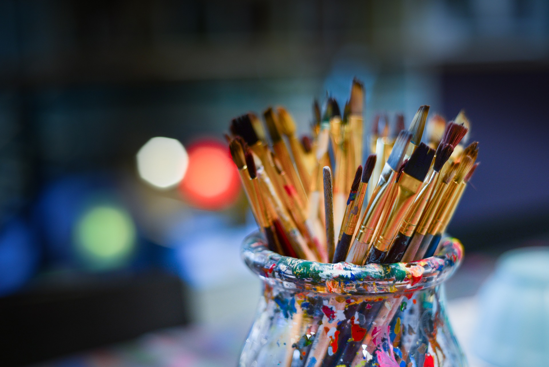 A stock photo of a glass with paint brushes in it and soft colorful lighting