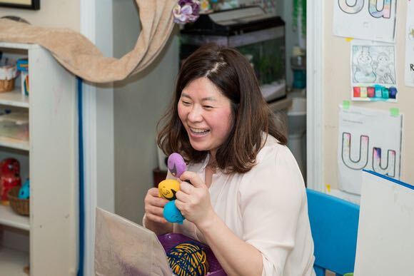 A smiling Korean woman with brown hair and a white shirt holds up a toy
