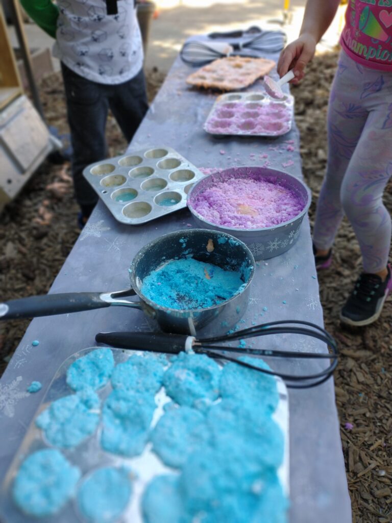 Children make colorful play cupcakes with blue and purple sand outdoors