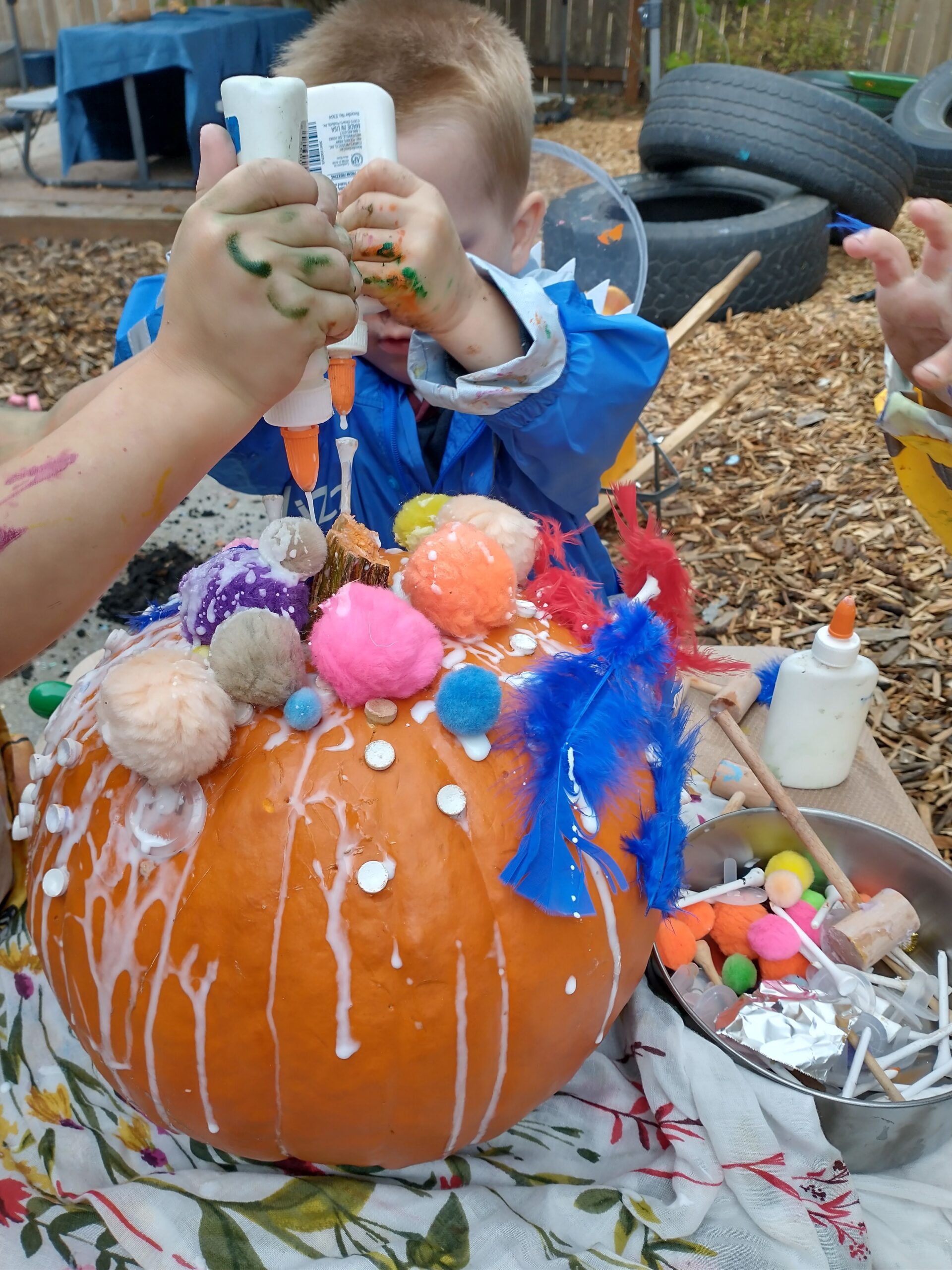 A child making a pumpkin craft with glue, feathers and pompoms