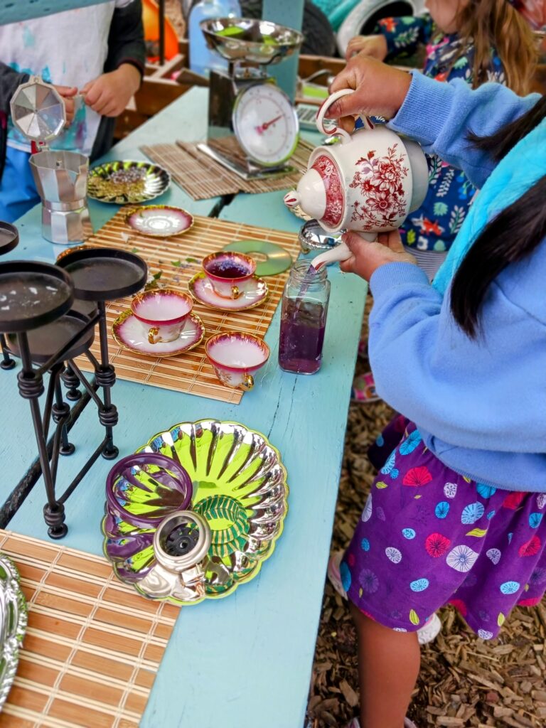 Children have a tea party with colorful dishes and a red and white teapot