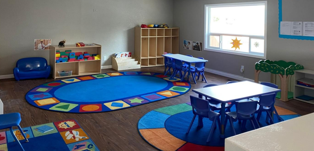 A photo of a home child care space with blue tables and chairs and colorful rugs