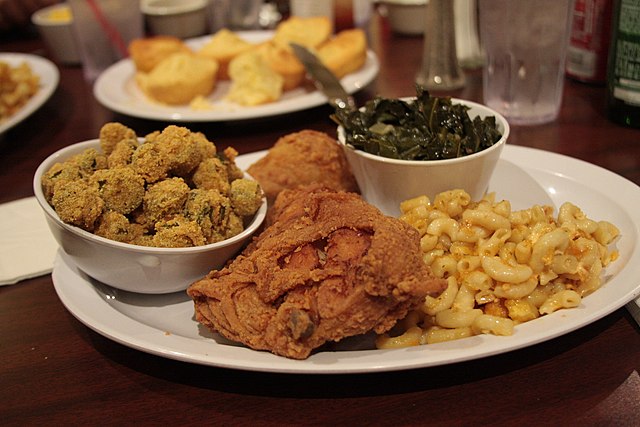 A plate with fried chicken, fried okra, macaroni and cheese, and collard greens