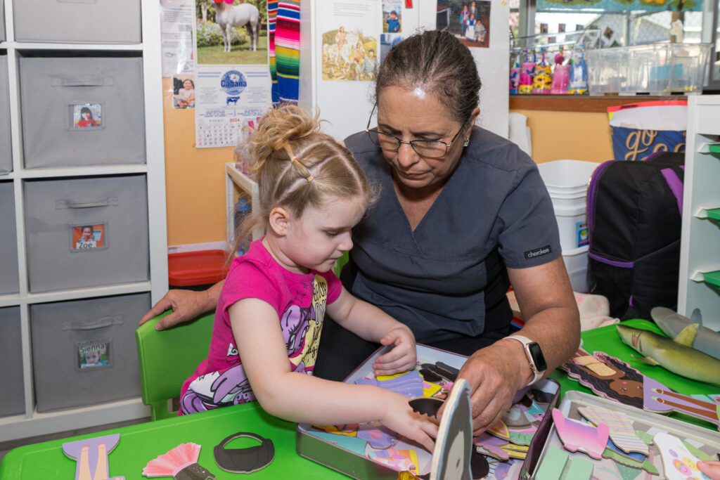 Amparo and a child in her care playing with dress-up dolls.